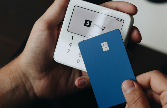 Hand holding a card payment terminal and a blue bank card