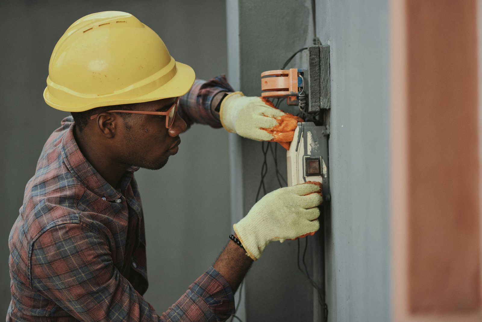 Electrician in hard hat working on a wall-mounted electrical panel