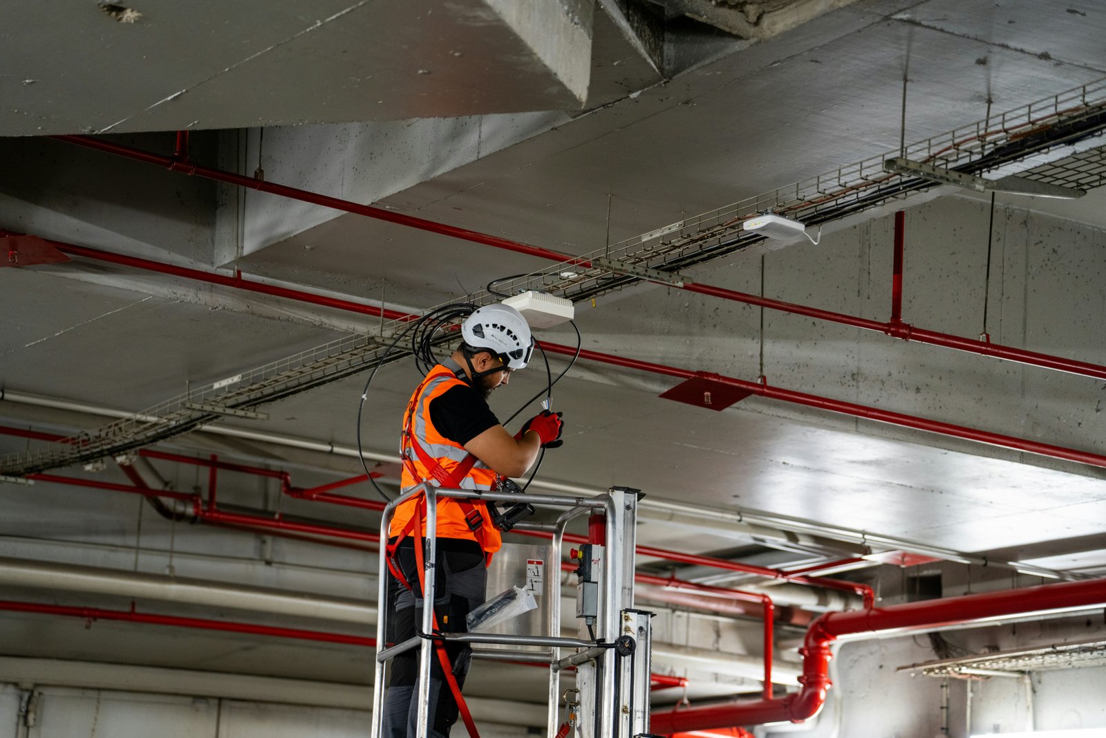 Technician in orange vest and hard hat on a lift installing cabling