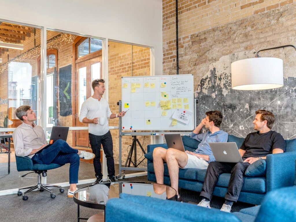 Colleagues with laptops watching a teammate present at a whiteboard