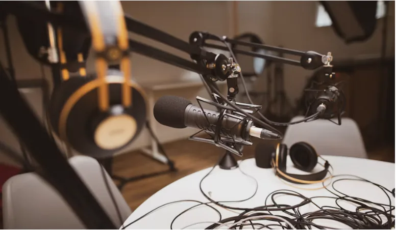Podcast studio microphone on a boom arm with headphones and cables on a round table