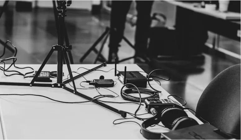 Black-and-white photo of a recording studio table with a tripod, audio recorder, cables and headphones