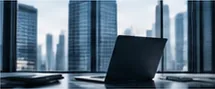 Laptop on a desk in front of a window overlooking city skyscrapers
