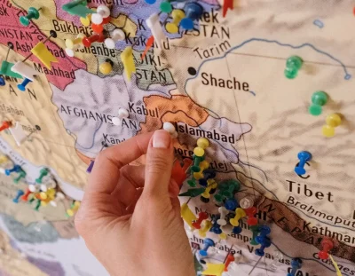 Hand placing pins on a colorful map highlighting new markets